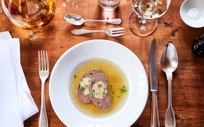 Milzroulade, Gedeck, Serviette, Weinglas, Rindsuppe, Kreuselpetersilie, Salzkörner, Holztisch