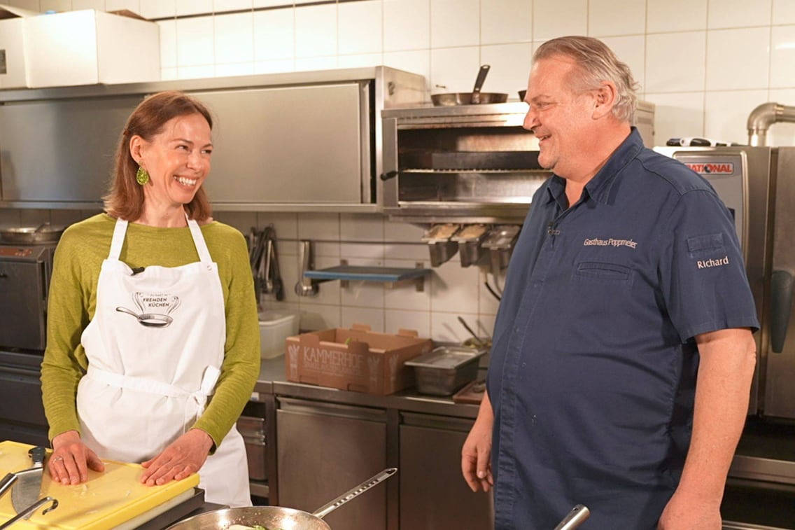 Doris Ahornegger mit Koch Richard Poppmeier in seiner Küche beim Herd.