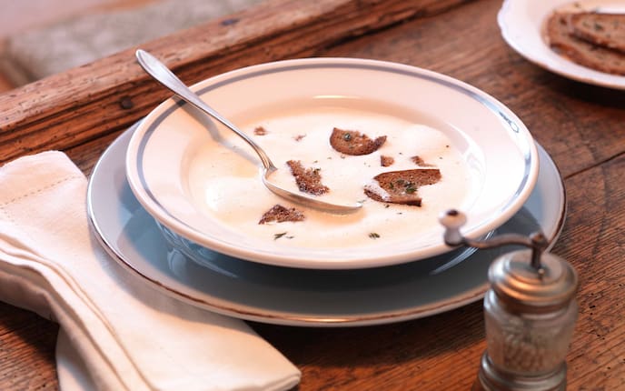 Geschäumte Bergkäsesuppe mit Kräuterkrusterl, Pfeffermühle, Stoffserviette, Gedeck, Holztisch