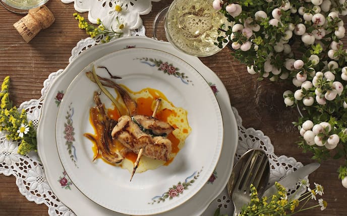 Altes Porzellangeschirr mit Blumen und Goldrand, Fleischteller unter dem Suppenteller, eingewickeltes Hühnerfilet mit einem Holzspieß zusammengesteckt, mit Sauce auf einem Holztisch